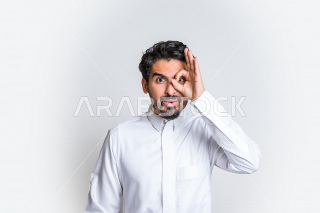 بورتريه لرجل عربي سعودي خليجي باللباس التقليدي , يقوم بإيماءات وجه مختلفة ، إشارات يد تدل على الرؤية بوضوح , الأهداف المستقبلية ، التركيز على شيء ما , خلفية بيضاء .