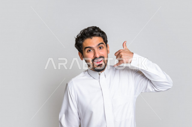 Portrait of a Saudi Gulf man in traditional dress, making different facial and hand gestures, a hand signal indicating receiving a call, a signal meaning call me, white background