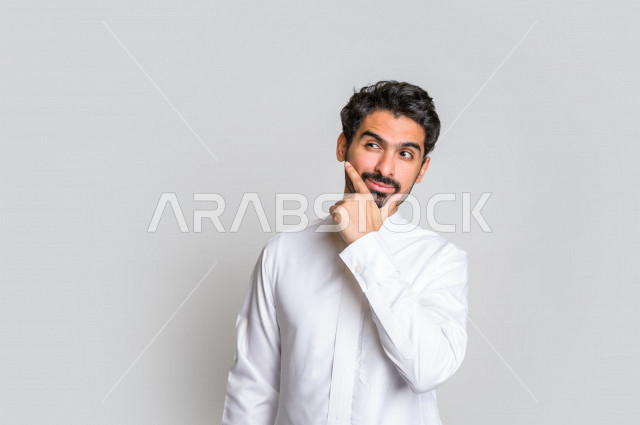 Portrait of a Saudi Gulf man in traditional dress, making facial and hands gestures that indicate thinking and bewilderment, white background