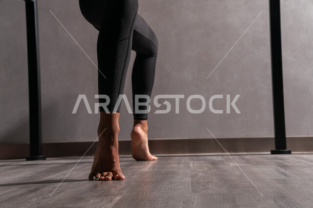 صوره من الخلف لإمرأه عربيه سعوديه خليجيه ترتدي الزي الرياضي , رياضة البيلاتس وحركات الاستطاله ، المحافظه على الصحه واللياقه الجسديه ، ممارسة رياضة الجمباز في النادي الرياضي النسائي