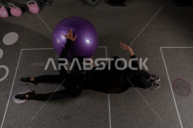 إمرأه عربيه سعوديه خليجيه ترتدي الزي الرياضي تقوم بممارسة التمارين الرياضية مع كرة بيلاتيس ، كرة اللياقة و التوازن ، نشاط بدني للمحافظة على الصحة و اللياقة الجسدية وتقوية عضلات الجسم ، أسلوب حياة صحي