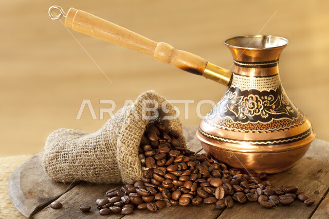 صورة مقربة لدلة قهوة وحبوب من البن المحمص المتناثرة , حبوب القهوة المبعثرة , مشروبات منشطة بالكافيين , حبات البن الداكنة , خلفية بنية . 