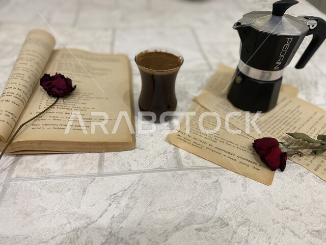 صورة مقربة لإبريق وكوب من القهوة بجانب كتاب على صفحاته ورود حمراء ,  الاستمتاع بقراءة الكتب و المشروبات الساخنة , ورد جوري أحمر ,  خلفيات بيضاء . 
