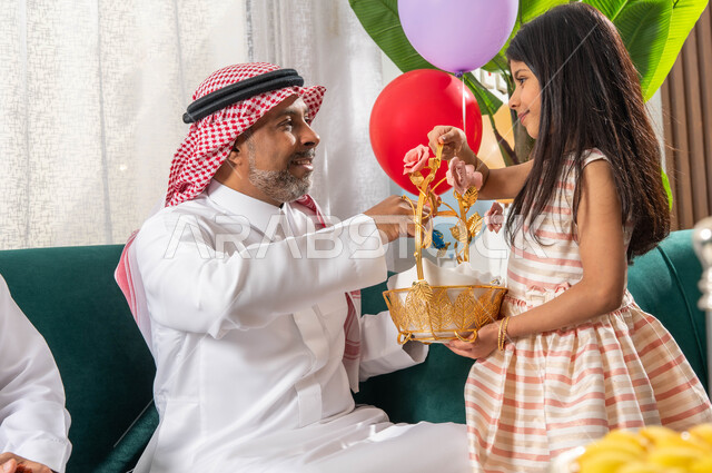 البهجة والفرحة بين الاقارب والاهل, صورة مقربة لفتاة عربية خليجية سعودية تقوم بتقديم قطع الشوكولاتة في مناسبة العيد السعيد, تجمع أسري لعائلة عربية خليجية سعودية في غرفة الجلوس يحتفلون في العيد,  أجواء العيد في المجتمع السعودي, حسن استقبال واكرام الضيف.