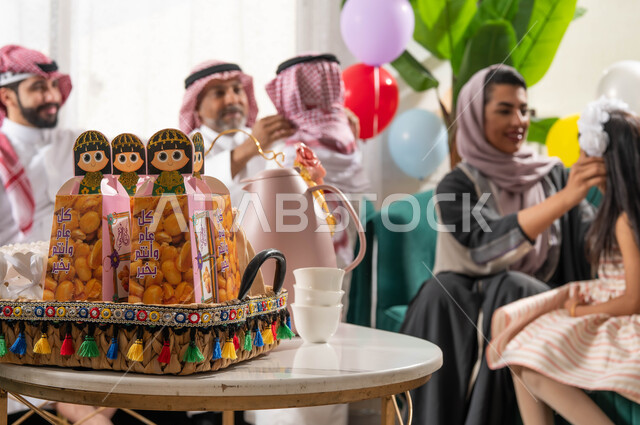 A close-up of the Eid distributions and the Qirqe’an basket, a family gathering for a Saudi Arabian Gulf family celebrating the Eid, the joy and joy between the family and relatives, gestures indicating joy and pleasure, the atmosphere of the Eid in the S