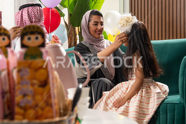 سلة قرقيعان وتوزيعات العيد, أم عربية خليجية سعودية تقوم بتصفيف شعر ابنتها و تحتفل في العيد السعيد ، إيماءات وجه تدل على الفرح والسعادة،  ديكورات وزينة الاحتفال, زيارات وتجمعات العيد في السعودية 