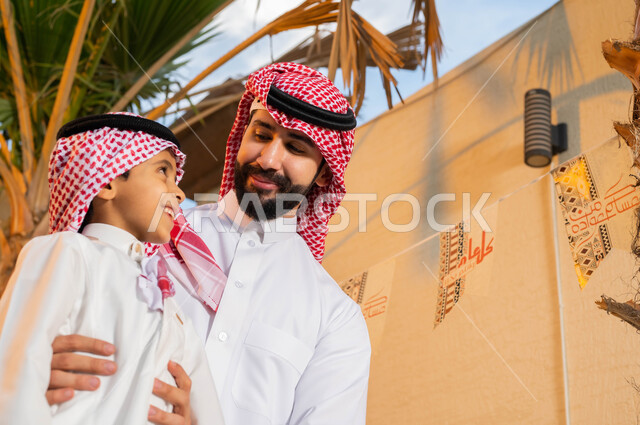 الاحتفال بقدوم العيد, صورة مقربة لرجل عربي خليجي سعودي مع ابنه يحتفلون في العيد, ديكورات وزينة العيد السعيد, أعياد ومناسبات اسلامية, ارتداء الثوب و الشماغ السعودي .