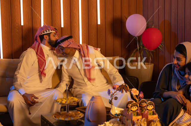 الزيارات والتجمعات الأسريه في الاعياد  والمناسبات الاسلامية, صورة مقربة لرجل عربي سعودي خليجي يرتدي الزي السعودي التقليدي يقوم بتقبيل رأس والده, أجواء عائليه سعيده, العيد المبارك