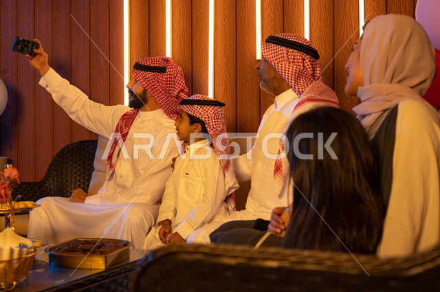 صور تذكارية في أيام العيد السعيد, صورة من الخلف  لعائلة عربية خليجية سعودية تحتفل بالعيد ,التقاط صور سيلفي عبر الهاتف المحمول، أعياد ومناسبات ، ارتداء اللباس السعودي التقليدي , الزيارات والتجمعات الاسريه