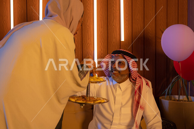 التهنئه بقدوم العيد في الأعياد والمناسبات الاسلامية السعيدة ,رجل عربي سعودي خليجي يرتدي الزي السعودي التقليدي , تقديم حلوى وكعك العيد , حسن استقبال واكرام الضيوف, ايماءات تدل على الفرح والسعاده, الزيارات و التجمعات الاسريه