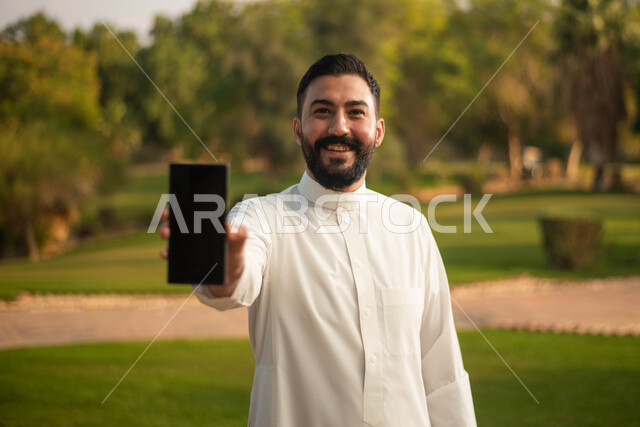 عرض شاشة سوداء فارغة ، رجل عربي خليجي سعودي يرتدي الزي السعودي التقليدي يقضي أوقات ممتعة في إحدى الحدائق في السعودية،  نزهه في الهواء الطلق، جولة في الطبيعة الخضراء