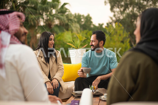 عطلة صيفية سعيدة وقضاء أوقات ممتعة برفقة الاصدقاء ، مجموعة من الشباب والبنات العرب الخليجيون السعوديون يستمتعون بتبادل الحديث في احد المقاهي في السعودية ، المشروبات الساخنة، دردشة وحوارات.