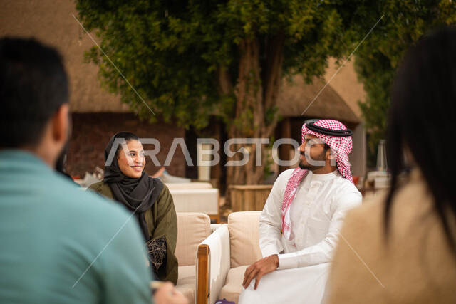 A group of Saudi Gulf Arab friends enjoying an exchange of conversation in a cafe in Saudi Arabia, cold drinks, a happy summer vacation, spending fun times with friends, chatting and dialogues.