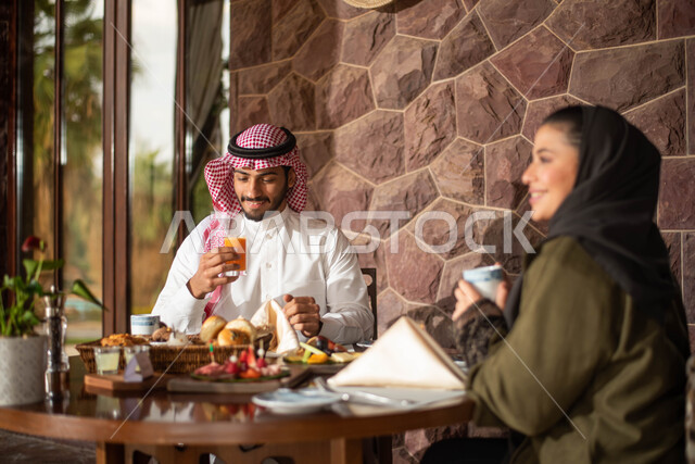 Gestures indicating joy and happiness, a Saudi Arabian Gulf couple enjoying eating in a Saudi restaurant, discussions and dialogues, spending pleasant times in a Saudi restaurant