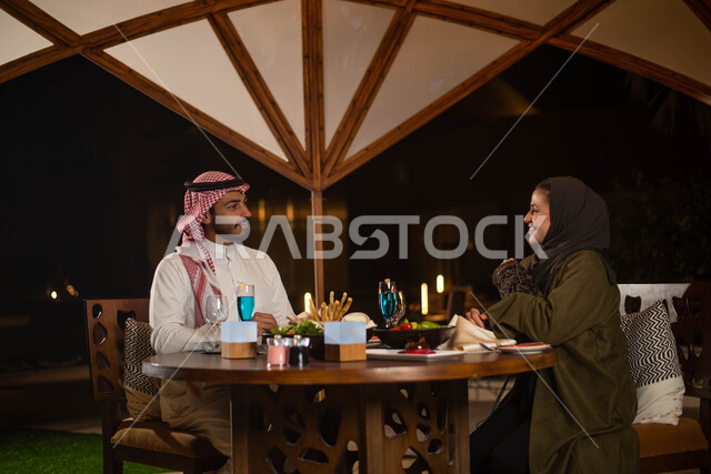 قضاء أوقات ممتعة ، رجل عربي خليجي سعودي يرتدي الزي السعودي التقليدي وأمرأة عربية خليجية سعودية ترتدي العباءة الخليجية السعودية يتناولان الطعام في إحدى المطاعم السعودية ، عطلة صيفية سعيدة ،  دردشة وحوارات