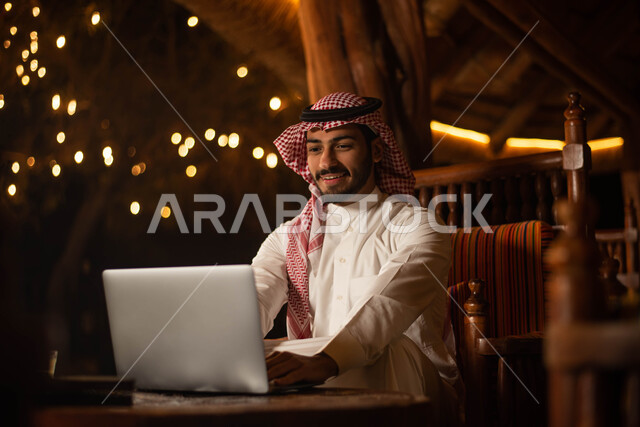 أجواء سعيدة ، تصفح الانترنت ، رجل سعودي عربي خليجي  يرتدي الزي التقليدي السعودي يقضي اوقات ممتعة في احد المقاهي في السعودية ، استخدم الهاتف المحمول بخلفية شاشة سوداء .