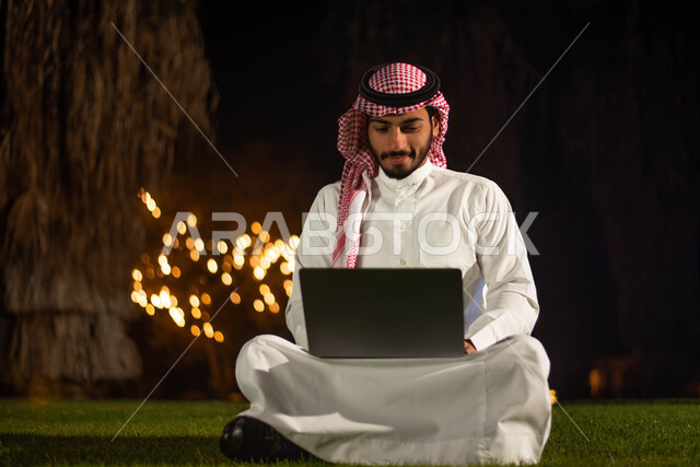  تصفح الإنترنت ، عقد إجتماع عمل عن بعد ، رجل عربي خليجي سعودي يرتدي الزي السعودي يستخدم الحاسوب المحمول ،   قضاء اوقات ممتعة في الهواء الطلق ، حدائق ومنتزهات.