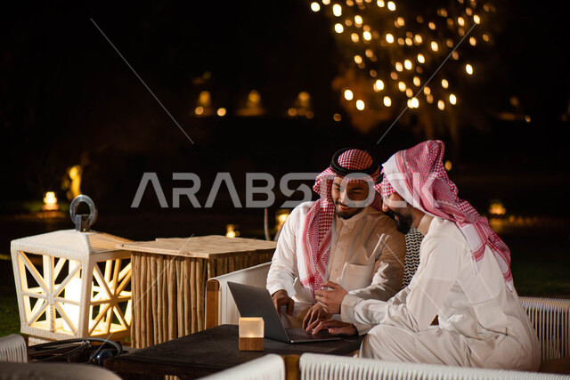  اجتماع رجال الأعمال ، رجلان عربيان خليجيان سعوديان يجلسان على الأريكة ، انجاز مهام العمل  عبر إستخدام جهاز الحاسوب المحمول ،  الحوارات والنقاشات ، تصفح الانترنت ، إستخدام أجهزة تقنية حديثة ، جلسات خارجية في الهواء الطلق.