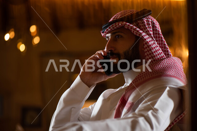 A close-up of a Saudi Arabian Gulf man wearing traditional Saudi clothing, completing work tasks and projects by making a phone call using a mobile phone, communicating with friends, the concept of business management.