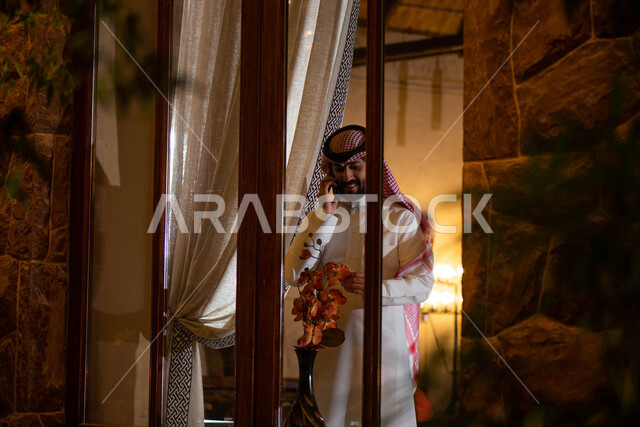 Accomplishment of work tasks and projects by making a phone call using a mobile phone, a Saudi Arabian Gulf man wearing traditional Saudi dress with gestures indicating happiness and pleasure, communication with friends, the concept of business management