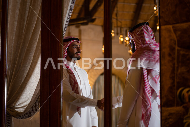 Greetings and peace, two Saudi Arabian Gulf men shaking hands happily, greeting and greeting between friends, hand gestures indicating shaking hands, spending pleasant times with friends, agreeing on a new business deal, business partners.