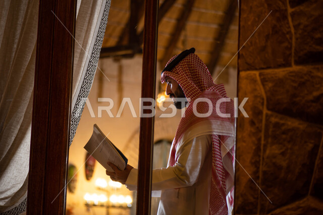 قضاء أوقات ممتعة في قراءة الكتب المفيدة للتعلم والتثقف  ، رجل عربي خليجي سعودي يرتدي الزي التقليدي السعودي يحمل بيده كتاب ، ممارسة هواية القراءة .