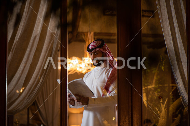 ممارسة هواية القراءة ، رجل عربي خليجي سعودي يرتدي الزي التقليدي السعودي يحمل بيده كتاب ،  قضاء أوقات ممتعة في قراءة الكتب المفيدة للتعلم والتثقف .