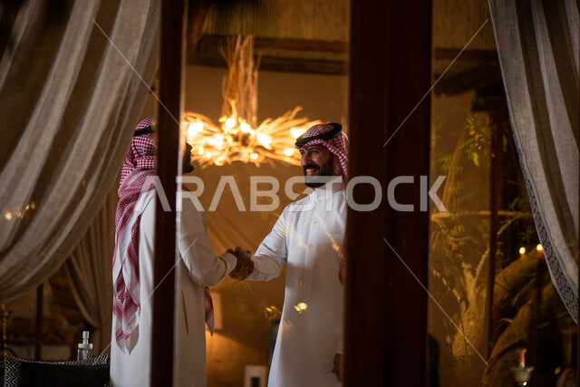 Greeting and greeting between friends, spending pleasant times with friends, two Saudi Arabian Gulf men shaking hands happily, hand gestures indicating handshake, greeting and peace, agreeing on a new business deal, business partners