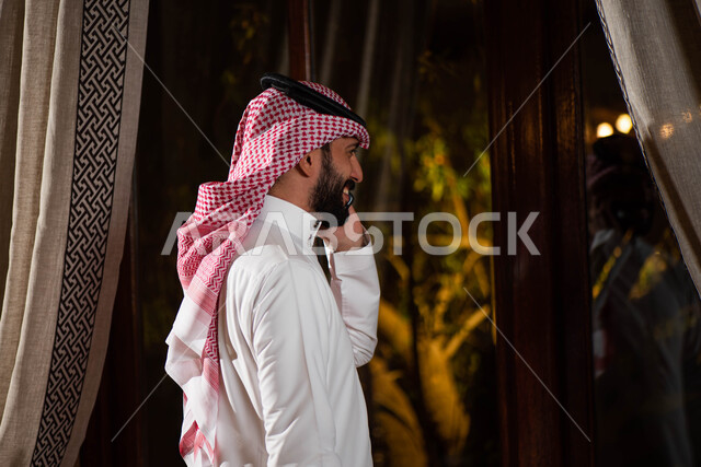 The concept of running a business and concluding business deals, a Saudi Arabian Gulf man wearing the traditional Saudi dress, communicating with friends, making a phone call using a mobile phone to complete work tasks and projects, gestures indicating ha