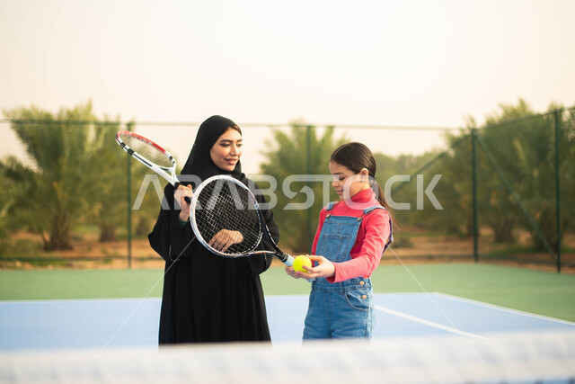 قضاء أوقات عائلية ممتعة ، اللعب والترفيه ، انشطة ترفيهية رياضية ، امرأة عربية خليجية سعودية ترتدي العباءة الخليجية السعودية تقضي اوقات ممتعة مع ابنتها ، ممارسة كرة التنس الارضي في ملعب رياضي
