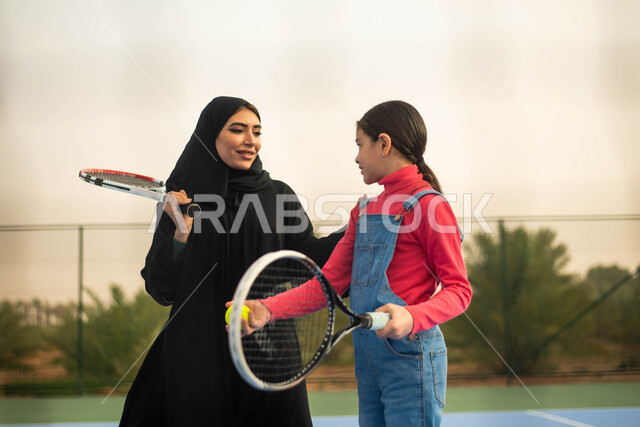 قضاء أوقات عائلية ممتعة ، اللعب والترفيه ، انشطة ترفيهية رياضية ، امرأة عربية خليجية سعودية ترتدي العباءة الخليجية السعودية تقضي اوقات ممتعة مع ابنتها ، ممارسة كرة التنس الارضي في ملعب رياضي