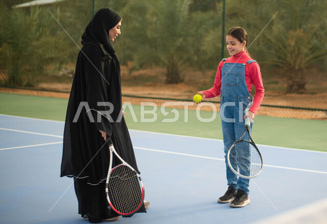 Spending fun family times, practicing tennis in a sports court, a Saudi Arab Gulf mother wearing the Saudi Gulf abaya, spending fun times with her daughter, sports entertainment activities, sports games, playing and entertainment