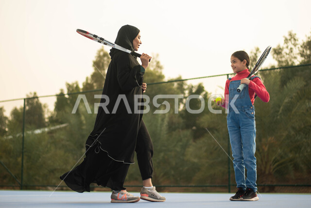 قضاء أوقات عائلية ممتعة ، ممارسة كرة التنس الارضي في ملعب رياضي ، أم عربية خليجية سعودية ترتدي العباءة الخليجية السعودية تقضي اوقات ممتعة مع ابنتها ، انشطة ترفيهية رياضية، العاب رياضية، اللعب والترفيه