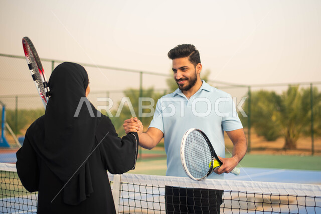 ايماءات وجه تدل على الفرح والسعادة قضاء أوقات عائلية ممتعة وممارسة كرة التنس الارضي، زوجان عربيان خليجيان سعوديان يتصافحان استعدادا لبدء لعب كرة المضرب،  ملعب رياضي وانشطة ترفيهية رياضية، العاب رياضية، اللعب والترفيه