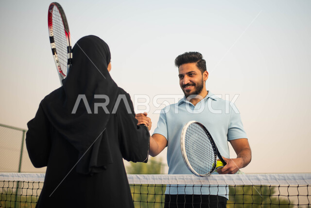 ايماءات وجه تدل على الفرح والسعادة قضاء أوقات عائلية ممتعة وممارسة كرة التنس الارضي، زوجان عربيان خليجيان سعوديان يتصافحان استعدادا لبدء لعب كرة المضرب،  ملعب رياضي وانشطة ترفيهية رياضية، العاب رياضية، اللعب والترفيه