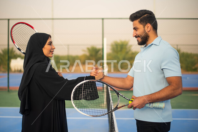 قضاء أوقات عائلية ممتعة ، ممارسة كرة التنس الارضي، زوجان عربيان خليجيان سعوديان يتصافحان استعدادا لبدء لعب كرة المضرب،  العاب رياضية، اللعب والترفيه