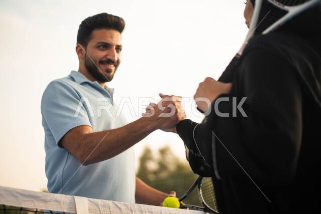 قضاء أوقات عائلية ممتعة ، ممارسة كرة التنس الارضي، زوجان عربيان خليجيان سعوديان يتصافحان استعدادا لبدء لعب كرة المضرب،  العاب رياضية، اللعب والترفيه