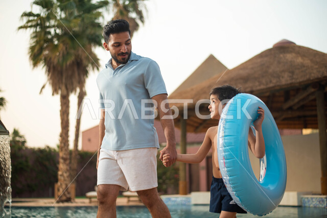 الاستعداد للسباحة في المسبح ، أب عربي خليجي سعودي يقضي اوقات ممتعة مع ابنه، اجواء صيفية ممتعة والمشي على حدود البركة المائية، رحلة سياحية ترفيهية واستخدام عوامة السباحة وقضاءعطلة صيفية سعيد
