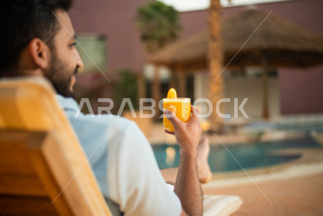 الجلوس على كرسي مريح ، صورة  من الخلف لرجل عربي خليجي سعودي يجلس على كرسي الاسترخاء في احدى المنتجعات ، عطلة صيفية والاستمتاع بشرب العصير الطازج ، وجهات سياحية ،  سياحة واستجمام