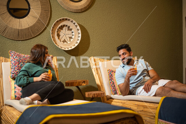 عطلة صيفية والاستمتاع بشرب العصير الطازج ، زوجان عربيان خليجيان سعوديان يجلسان على كرسي الاسترخاء في احدى المنتجعات السياحية ، وجهات سياحية ، منتجع سياحي سياحة واستجمام.