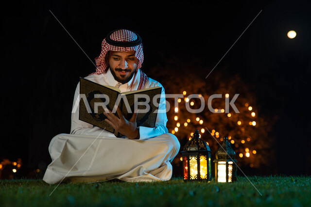 قراءة وتلاوة وحفظ القرآن الكريم، إضاءة وزينة شهر رمضان ، رجل عربي خليجي سعودي يرتدي الزي السعودي التقليدي يحمل بيده المصحف الشريف، شهر رمضان المبارك وأجواء رمضانية