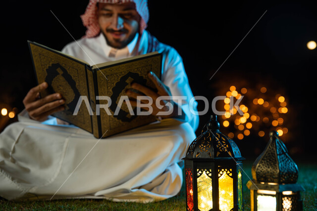 إضاءة وزينة شهر رمضان ، رجل عربي خليجي سعودي يرتدي الزي السعودي التقليدي يحمل بيده المصحف الشريف، قراءة وتلاوة وحفظ القرآن الكريم، شهر رمضان المبارك وأجواء رمضانية