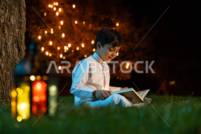 حفظ وقراءة وتلاوة القرآن الكريم،  طفل عربي خليجي سعودي يرتدي الزي السعودي يمسك المصحف الشريف ، ذكر الله في شهر رمضان المبارك ، إضاءة وزينة شهر رمضان