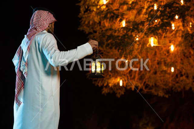 Religious occasions, Islamic rituals and worship, a picture from behind of a Saudi Arabian Gulf man wearing the traditional Saudi dress holding the Ramadan lantern, lighting and decorations for the month of Ramadan, Ramadan atmosphere, the blessed month o