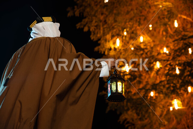 اليوم الوطني السعودي، تراثيات وشعبيات ، أجواء رمضانية، مناسبات دينية ، اسلاميات وعبادات ، صورة من الخلف لرجل عربي سعودي خليجي يرتدي الزي التراثي الشعبي التقليدي يمسك بيده فانوس رمضان ، النظر الى شيء ما، يوم التاسيس السعودي ، إضاءة وزينة شهر رمضان