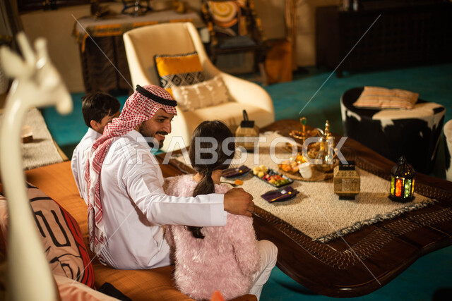 فانوس رمضان، ايماءات وجه تدل على السعادة والسرور ، استقبال شهر رمضان المبارك ، عائلة عربية خليجية سعودية تحتفل بقدوم رمضان المبارك في غرفة المعيشة ، دلة القهوة العربية  ، مشروبات ساخنة وحلوى رمضان
