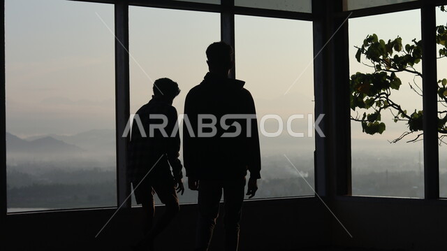 صورة ظلية لرجلان يقفان أمام النافذة  داخل المبنى, النظر وتأمل الطبيعه من النافذه,  مناظر طبيعيه من الأبراج والمباني المرتفعه , سيلوليت