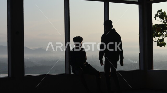 صورة ظلية لرجلان يقفان أمام النافذة  داخل المبنى, النظر وتأمل الطبيعه من النافذه,  مناظر طبيعيه من الأبراج والمباني المرتفعه , سيلوليت