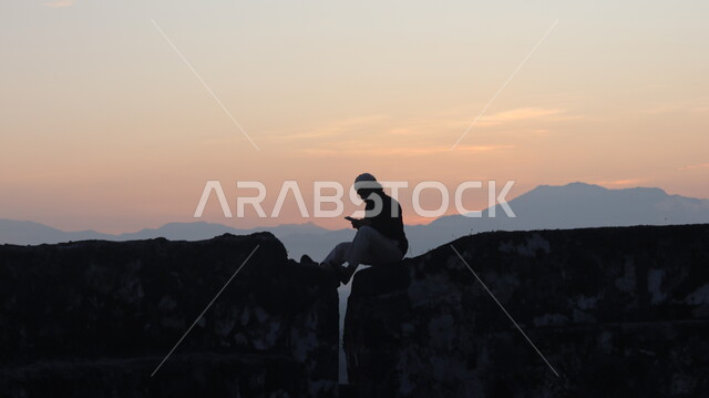 صورة ظلية لشاب يجلس فوق جبل صخري، الجبال والمرتفعات وقت غروب الشمس، القمم الجبلية الصخرية، مناظر طبيعية، خلفية الطبيعة