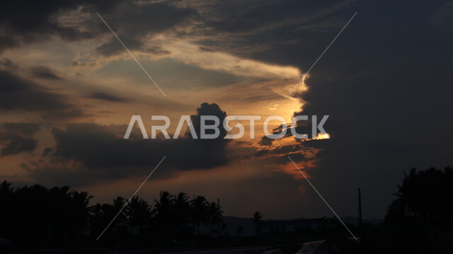 صورة ظلية لاشجار النخيل وقت غروب الشمس، الشماء الملبدة بالغيوم، الشمس المغطاة بالغيوم السوداء، ظهور الشفق الاحمر، خلفية الطبيعة